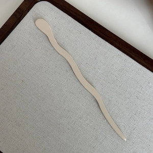 Close-up of a minimalist cream acetate wavy hair stick on a grey fabric display tray