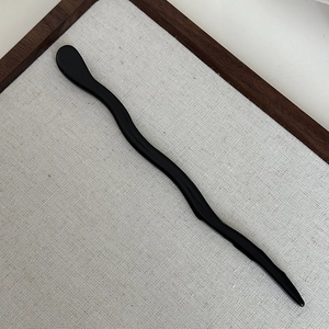 Detail shot of a black wave-shaped acetate hair pin with a polished S-curve design