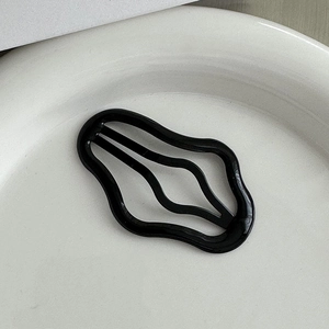 Dettaglio macro della molletta nera ondulata su un vassoio di ceramica bianca