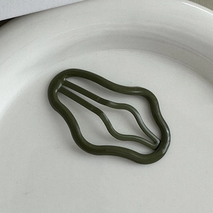 Dettaglio del fermaglio per capelli ondulato verde oliva su un piatto di ceramica