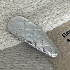 Detail of silver quilted faux leather Y2K hair clip with metallic finish on knit fabric