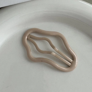 Dettaglio di un fermaglio per capelli ondulato opaco color tè al latte su vassoio
