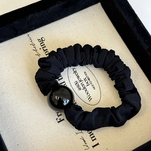 Détail d'un chouchou plissé noir orné d'une grande perle ronde noire polie