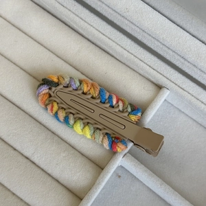 Detailed close-up of colorful woven wool hair clips on a soft grey jewelry tray