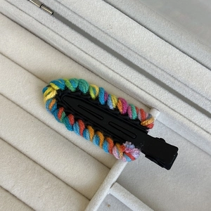 Detailed close-up of rainbow knitted wool yarn wrapped around a black metal hair clip