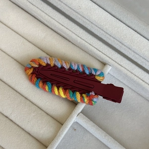 Detail view of colorful hand-woven yarn hair clip on a soft gray velvet display