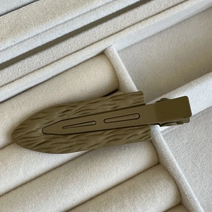 Dettaglio della molletta per capelli verde oliva con trama foglia su vassoio grigio