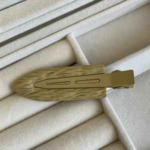 Dettaglio del fermaglio a becco d'anatra opaco color kaki su portagioie in velluto grigio