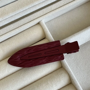 Dettaglio di fermaglio per capelli bordeaux opaco con trama a piuma su velluto grigio