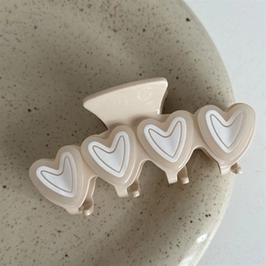 Detail of cream hair claw clip with layered white heart patterns on ceramic tray