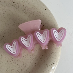 Close-up of pink hair claw clip featuring purple and white heart-shaped patterns