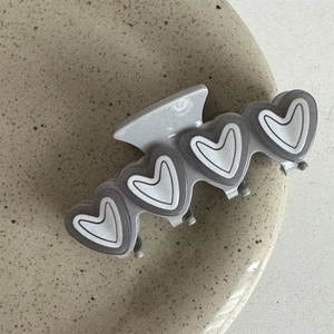 Detail of grey heart-shaped claw clip with matte finish on a minimalist ceramic plate