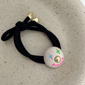 Detail of black elastic hair tie featuring a cute cream star-eye smile face pendant