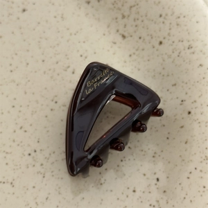Detailed close-up of dark brown tortoiseshell acetate hair clip with gold text