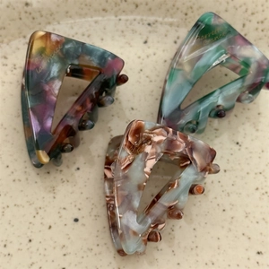 Close-up of three triangle acetate hair claws with marble texture and gold lettering detail