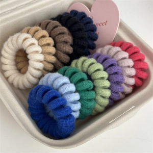 Close-up of 12 multi-colored knitted spiral hair ties neatly arranged in a paper gift box