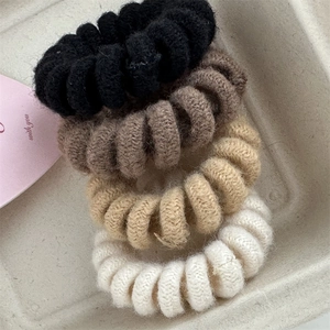 Close-up of four knitted spiral hair ties in neutral earth tones with wool texture