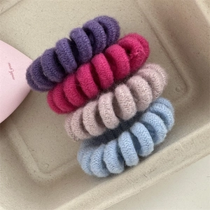 Close-up of four candy-colored knitted spiral hair ties in a minimalist beige tray