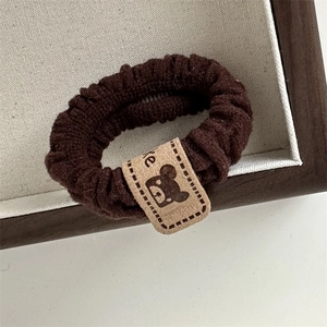 Close-up of brown knitted elastic hair tie with a cute bear tag for high ponytails