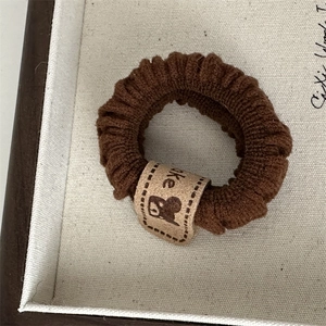 Close-up of dark brown knitted hair scrunchie with cute bear label and cake text