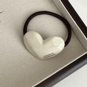 Detail of high-elasticity hair tie with a creamy white acetate heart-shaped charm