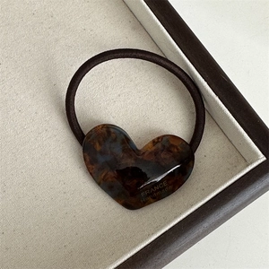 Detailed view of tortoiseshell acetate heart pendant on elastic hair tie with gold lettering