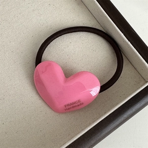 Close-up of pink acetate heart hair tie with France Handmade text on beige tray