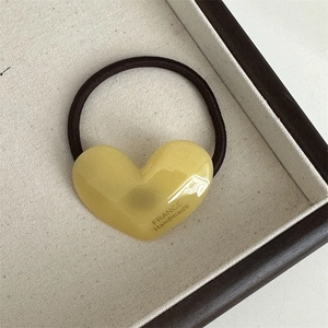 Close-up of yellow acetate heart hair tie with France Handmade text on wooden tray