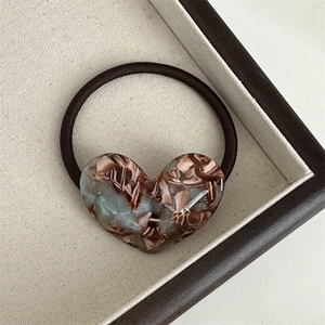 Macro shot of acetic acid heart charm hair tie on a brown wooden tray background