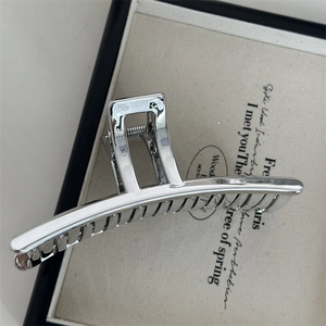 Détail d'une grande pince à cheveux en métal argenté avec finition miroir sur tissu beige