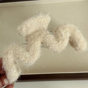 Dettaglio macro della molletta a onde beige in peluche con consistenza morbida