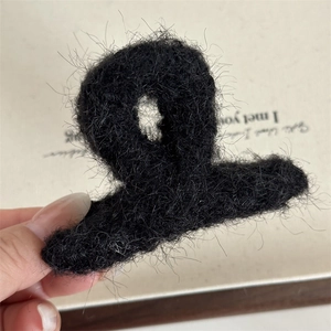 Dettaglio della soffice consistenza in peluche nero e design curvo della clip a molla