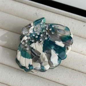 Macro detail of shell-shaped acetate hair claw with marble texture and rhinestones