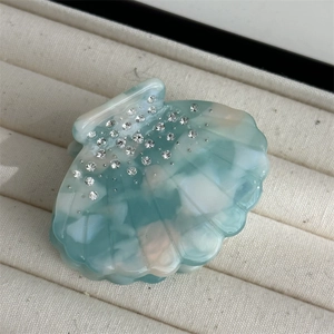 Detail view of scallop hair claw with teal marble texture and sparkling rhinestones
