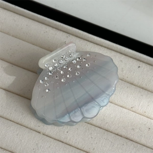 Detailed close-up of shell-shaped hair claw with rhinestones on beige velvet tray