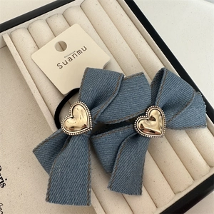 Detail von blauen Denim-Haarschleifen mit goldenen Herzanhängern und braunen Nähten