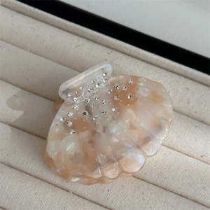 Detail of shell-shaped hair claw clip with pearlescent resin and sparkling rhinestones