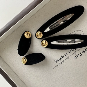 Elegant set of four black velvet hair clips with gold metal buttons on beige tray