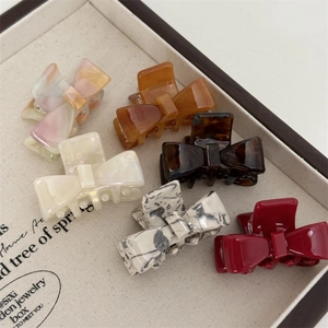 Elegant bow hair claws in acetate finishes like amber, cream white, and marble patterns