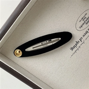 Close-up of a black velvet hair clip with a gold button accent on a display tray