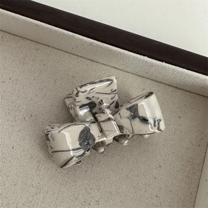Detail of a creamy white bow hair claw clip with black marble ink pattern in a tray