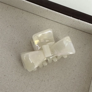 Detail of a pearl white marble texture bow hair claw clip on a beige fabric tray
