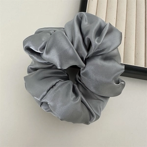 Détail macro du chouchou en satin argenté montrant la texture de soie et le design plissé