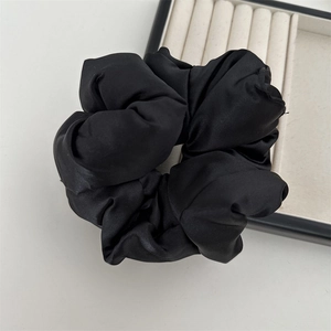 Détail d'un chouchou large en satin noir avec un éclat soyeux et une texture plissée
