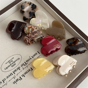 Macro display of heart-shaped acetate hair claws in nine various marble and amber patterns