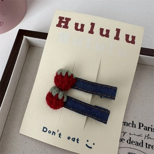 Détail de deux barrettes fraises avec denim bleu et décorations de baies rouges tricotées