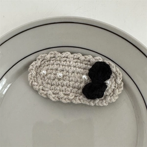 Detailed macro view of crochet hair clip featuring white pearls and a black knit bow