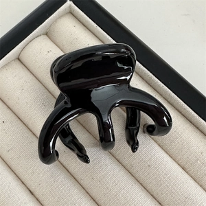 Detail of the high-gloss black claw clip with rounded teeth on a soft velvet tray