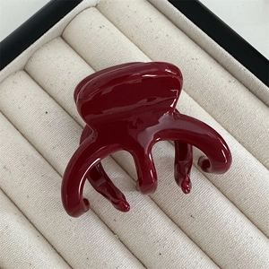Macro shot of dark red glossy hair claw clip resting on a textured display tray