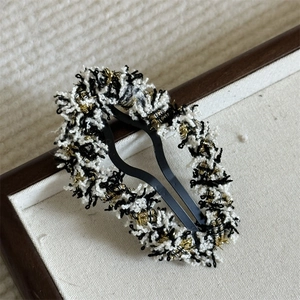 Detail of tweed fabric hair clip with black gold weaving on a textured display